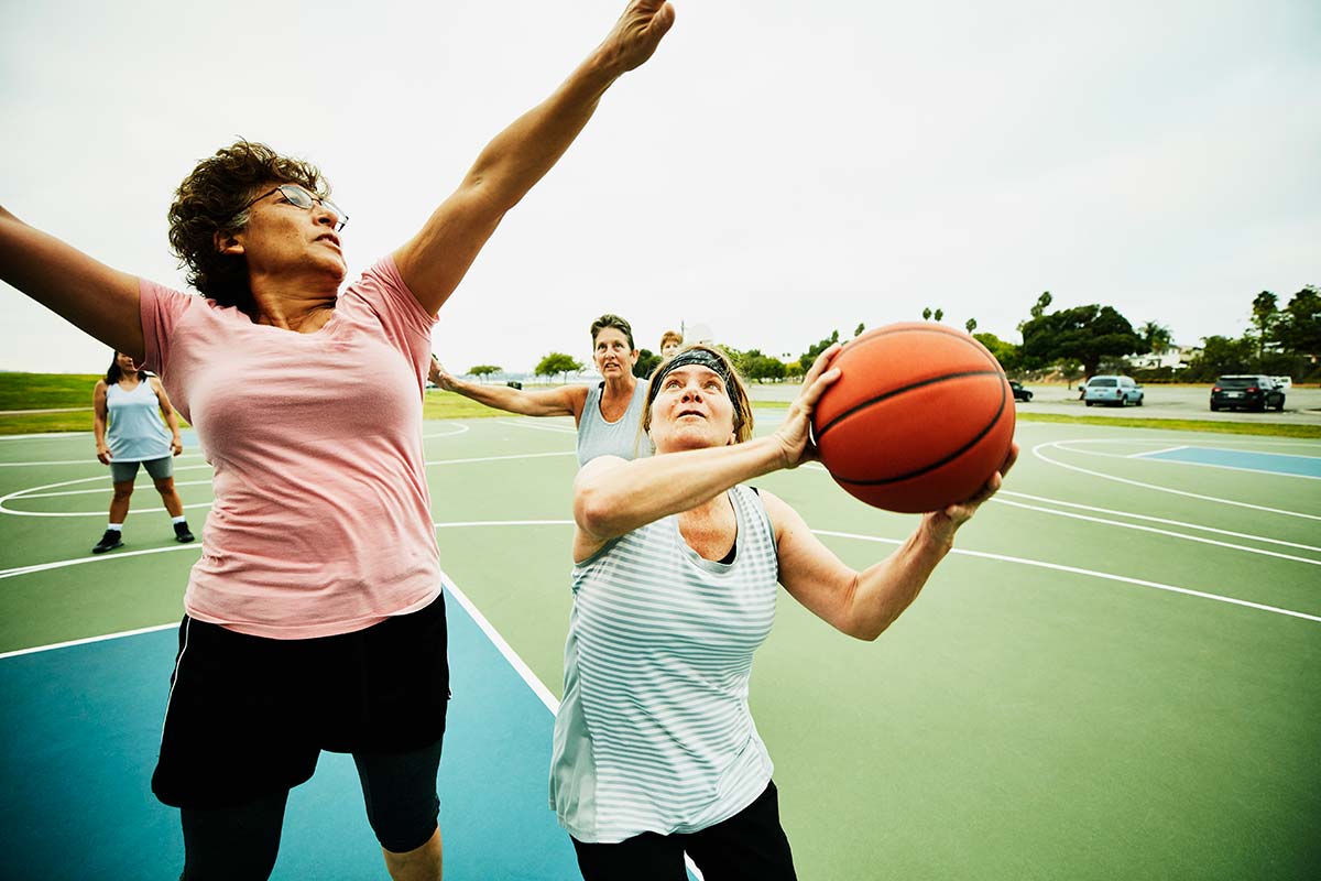 Ett gäng medelålderskvinnor spelar basket ute på en plan